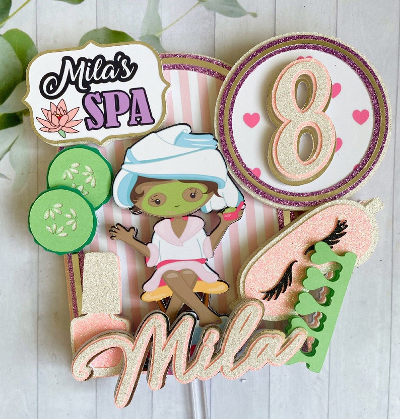 Puede incluir: Adorno para tarta con tem&aacute;tica de spa. Presenta una ni&ntilde;a de dibujos animados con mascarilla, rodajas de pepino y el texto "Mila's SPA". Tambi&eacute;n incluye el n&uacute;mero "8", junto con detalles de purpurina rosa y dorada.