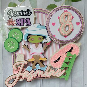 Puede incluir: Adorno para tarta con tem&aacute;tica de spa con el texto "Jasmine's SPA" y un personaje de dibujos animados con mascarilla y toalla. El adorno incluye un fondo a rayas rosas y blancas, rodajas de pepino y el n&uacute;mero 8 con corazones.