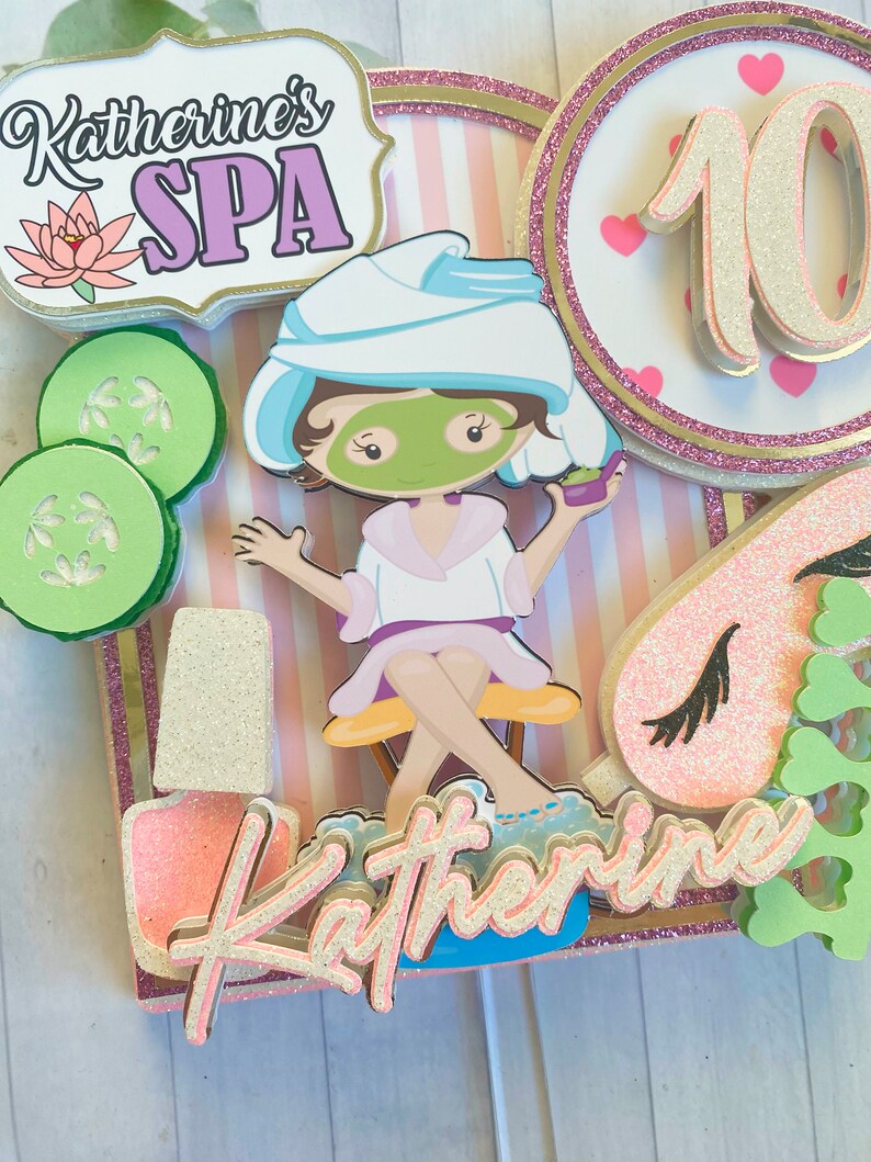 Puede incluir: Adorno para tarta con tem&aacute;tica de spa que presenta a una ni&ntilde;a de dibujos animados con mascarilla, pepinos y esmalte de u&ntilde;as. El adorno incluye el texto "Katherine's SPA" y el n&uacute;mero 10, con detalles en rosa y dorado.
