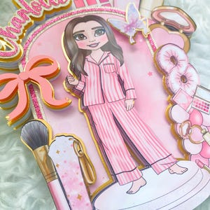 Personalized makeup-themed cake topper featuring a girl in pink striped pajamas surrounded by beauty and spa accessories including makeup brushes, lipstick, blusher, eyeshadow, skincare items, and a pink bow. The topper is decorated in pink glitter card and gold mirror  with the name and age of the birthday girl, making it perfect for a glam birthday, spa party, or makeup-themed celebration.