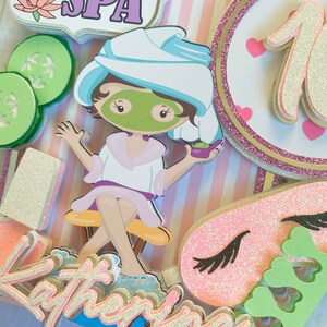 Puede incluir: Adorno para tarta con tem&aacute;tica de spa con el texto "Katherine's SPA". El adorno presenta una ni&ntilde;a de dibujos animados con una mascarilla, rodajas de pepino y un fondo a rayas rosas y blancas. Tambi&eacute;n incluye el n&uacute;mero 10 y una m&aacute;scara para dormir.