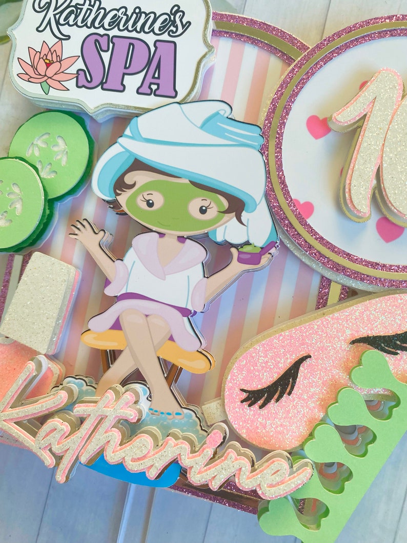 Puede incluir: Adorno para tarta con tem&aacute;tica de spa con el texto "Katherine's SPA". El adorno presenta una ni&ntilde;a de dibujos animados con una mascarilla, rodajas de pepino y un fondo a rayas rosas y blancas. Tambi&eacute;n incluye el n&uacute;mero 10 y una m&aacute;scara para dormir.