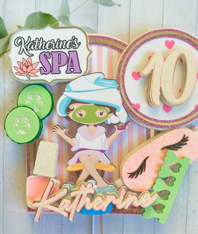 Puede incluir: Un adorno para pastel con tem&aacute;tica de spa que presenta a una ni&ntilde;a de dibujos animados con una mascarilla, pepinos, esmalte de u&ntilde;as y una m&aacute;scara para dormir. El adorno incluye el texto "Katherine's SPA" y el n&uacute;mero 10, con detalles en rosa y dorado.