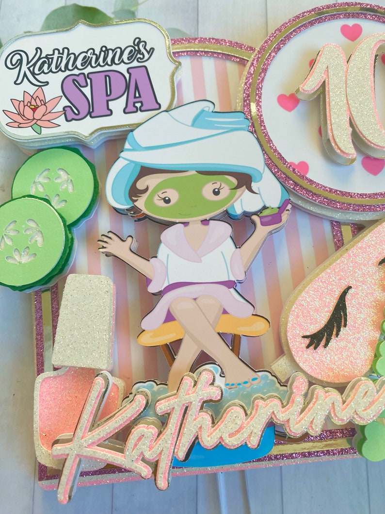 Puede incluir: Adorno para tarta con tem&aacute;tica de spa con el texto "Katherine's SPA" y un personaje de dibujos animados con mascarilla y toalla. Incluye rodajas de pepino, un frasco de esmalte de u&ntilde;as y el n&uacute;mero 10. Acentos rosas, blancos y dorados.