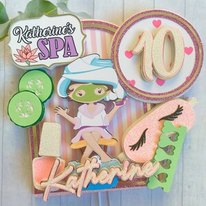 Puede incluir: Adorno para tarta con tem&aacute;tica de spa con el texto "Katherine's SPA" y una ni&ntilde;a de dibujos animados con una mascarilla. El adorno incluye el n&uacute;mero 10, rodajas de pepino y una m&aacute;scara para dormir rosa. El dise&ntilde;o presenta detalles en rosa, blanco, verde y purpurina dorada.