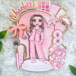 Personalized makeup-themed cake topper featuring a girl in pink striped pajamas surrounded by beauty and spa accessories including makeup brushes, lipstick, blusher, eyeshadow, skincare items, and a pink bow. The topper is decorated in pink glitter card and gold mirror  with the name and age of the birthday girl, making it perfect for a glam birthday, spa party, or makeup-themed celebration.