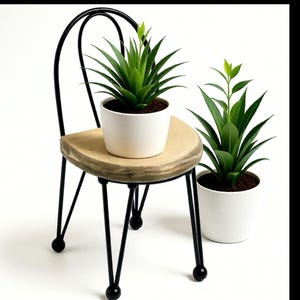 May include: A miniature chair with a round wooden seat and black metal frame. A white pot with a green plant sits on the chair. Another white pot with a green plant is beside the chair.