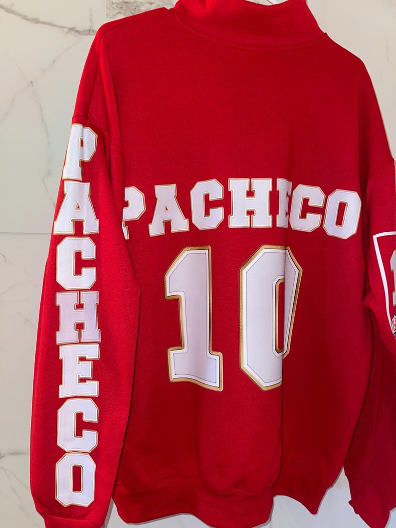 Puede incluir: Sudadera roja con el nombre "PACHICO" en letras blancas en la espalda y en la manga izquierda. El n&uacute;mero "10" est&aacute; debajo del nombre. Las letras y el n&uacute;mero tienen un contorno dorado.