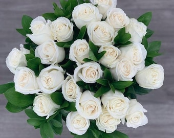 May include: A bouquet of white roses with green leaves.