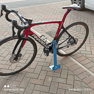 K&ouml;nnte beinhalten: Ein rotes und schwarzes Pinarello Rennrad mit einem blauen Fahrradst&auml;nder. Das Fahrrad hat einen schwarzen Lenker, schwarze R&auml;der und einen schwarzen Sattel.