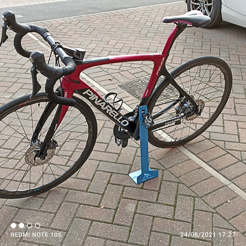 K&ouml;nnte beinhalten: Ein rotes und schwarzes Pinarello Rennrad mit einem blauen Fahrradst&auml;nder. Das Fahrrad hat einen schwarzen Lenker, schwarze R&auml;der und einen schwarzen Sattel.