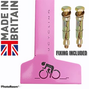 K&ouml;nnte beinhalten: Ein rosafarbener Fahrradhalter aus Metall mit einer Aussparung f&uuml;r einen Radfahrer auf einem Fahrrad. Der Halter ist f&uuml;r die Wandmontage konzipiert. Der Text "Cycling" ist vertikal auf dem Halter aufgedruckt. Zwei goldfarbene D&uuml;bel sind im Lieferumfang enthalten. Der Text "Fixing Included" ist unter den D&uuml;beln aufgedruckt.