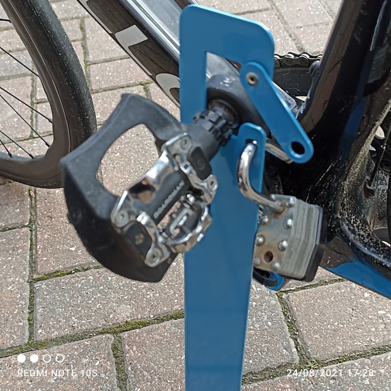 K&ouml;nnte beinhalten: Ein blauer Fahrradst&auml;nder aus Metall mit einem daran befestigten Fahrrad. Das Fahrrad hat einen schwarzen Rahmen und ein schwarzes und silbernes Pedal.