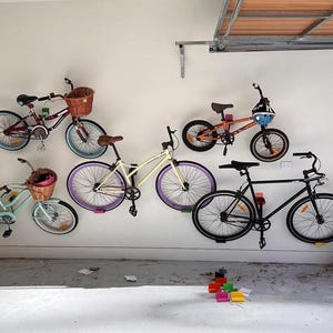 May include: Five bicycles are mounted on a white wall. The bicycles are in various colors, including black, white, red, and blue. The bicycles have different styles, including a cruiser, a mountain bike, and a road bike.