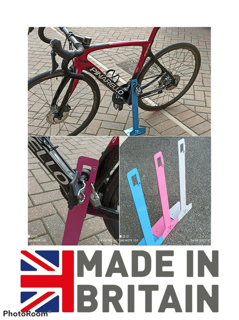 K&ouml;nnte beinhalten: Ein rotes und schwarzes Fahrrad lehnt an einem rosafarbenen Fahrradst&auml;nder aus Metall. Der Fahrradst&auml;nder ist mit "MADE IN BRITAIN" beschriftet.