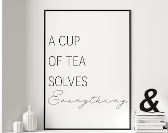 May include: Black and white typography print with the text "A cup of tea solves everything" in a minimalist style. The print is framed in a black frame and is displayed on a white wall.