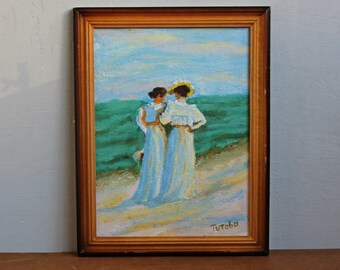 May include: A framed oil painting depicting two women in long white dresses walking on a sandy beach. The sky is blue and the water is turquoise. The painting is signed "Turtaba" in the bottom right corner.