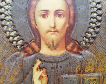 May include: A vintage religious icon depicting Jesus Christ with a halo, holding a book. The icon is framed in a metal frame with a decorative design.