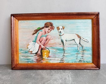 May include: A framed painting of a young girl in a white dress playing on a beach with a dog. The girl is holding a yellow bucket and the dog is white with brown spots. The painting is set against a blue sky and ocean background.