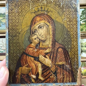 May include: A vintage religious icon depicting the Virgin Mary holding the baby Jesus. The icon is painted on a wooden panel and features a gold background with intricate details. The Virgin Mary is wearing a blue robe and a crown, while the baby Jesus is wearing a white robe.
