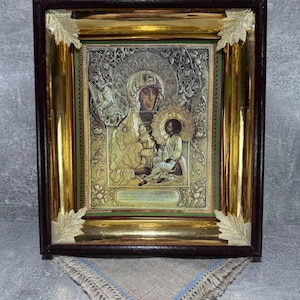 Könnte beinhalten: Eine gerahmte religiöse Ikone mit einem goldenen und braunen Rahmen. Die Ikone zeigt die Jungfrau Maria, die ein Jesuskind hält. Die Ikone ist von aufwendigen goldenen Details umgeben.