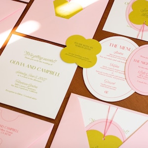 May include: A wedding stationery set featuring square and oval cards with pink and white paper, gold foil text, and mustard yellow clover-shaped tags. The text includes Olivia and Campbell, The Menu, and The Night Before, with pink envelopes.