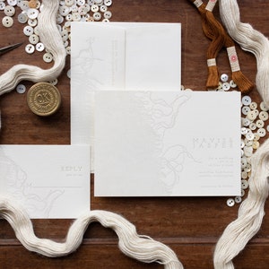 May include: A white wedding invitation suite with a delicate floral design. The invitation features the names "Mavis & Jasper" and includes details about the wedding ceremony and reception. The suite also includes a reply card.