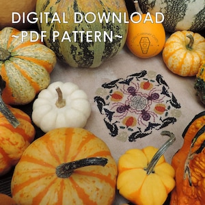 May include: A digital PDF pattern surrounded by various pumpkins. The pattern features a cross-stitch design with spiders, bats, and a spiderweb. The pumpkins are in shades of orange, yellow, green, and white, creating an autumnal theme.