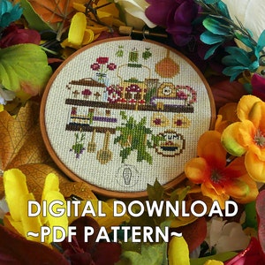 May include: A cross-stitch pattern featuring a whimsical kitchen scene with a shelf filled with various items, including a teapot, mugs, jars, and a bowl of fruit. The pattern is surrounded by a wooden embroidery hoop and a variety of colorful flowers.