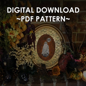 May include: A digital download PDF pattern for a cross stitch design featuring a ghost with a speech bubble that says "BOO" in a gold oval frame. The frame is surrounded by dried flowers and other fall decor.