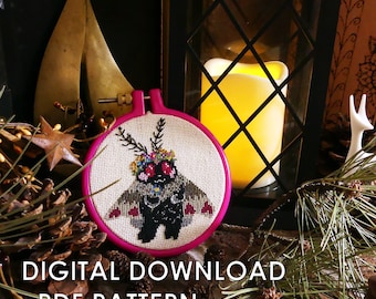 Op de afbeelding: Een roze borduurring met witte stof erin. De stof heeft een kruissteekontwerp van een mot met een bloemenkroon en hartvormige vleugels. De tekst "DIGITAL DOWNLOAD ~PDF PATTERN~" staat onder de ring.