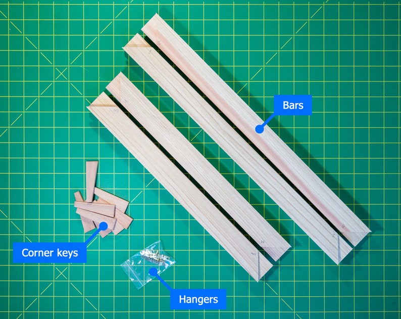 May include: Three wooden bars, corner keys, and hangers for a picture frame. The bars are light brown and the corner keys are small, triangular pieces of wood. The hangers are metal and are in a clear plastic bag.