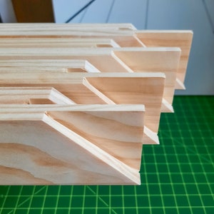 Puede incluir: Primer plano de una pila de barras de bastidor de lienzo de madera, que muestra las esquinas entrelazadas y la veta de madera natural. Las barras est&aacute;n dispuestas en un patr&oacute;n escalonado, con la barra superior ligeramente desplazada de la que est&aacute; debajo.