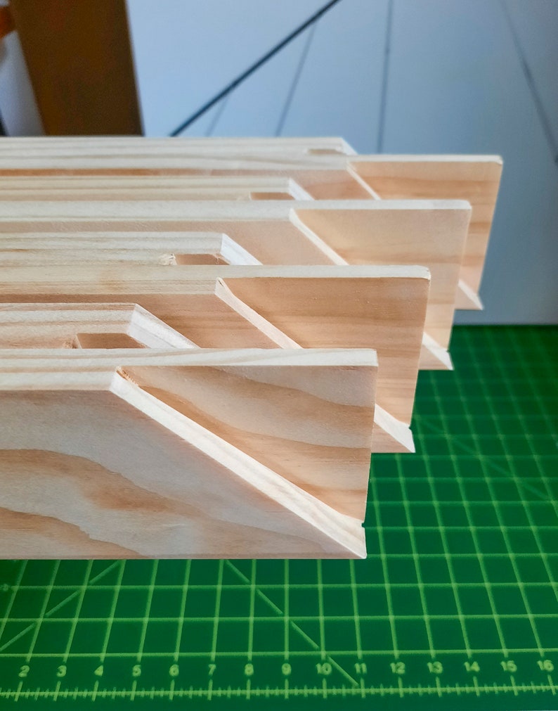 Puede incluir: Primer plano de una pila de barras de bastidor de lienzo de madera, que muestra las esquinas entrelazadas y la veta de madera natural. Las barras est&aacute;n dispuestas en un patr&oacute;n escalonado, con la barra superior ligeramente desplazada de la que est&aacute; debajo.