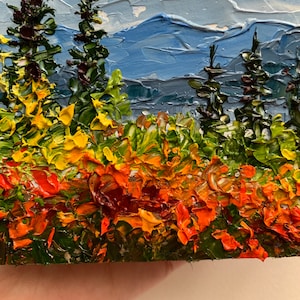 Op de afbeelding: Een schilderij van een landschap met een bergketen op de achtergrond en een veld met gele, oranje en rode bloemen op de voorgrond. Er staan ook een paar groene bomen op de voorgrond.