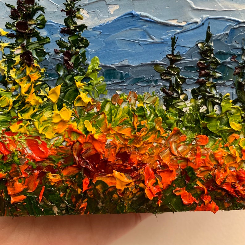 Op de afbeelding: Een schilderij van een landschap met een bergketen op de achtergrond en een veld met gele, oranje en rode bloemen op de voorgrond. Er staan ook een paar groene bomen op de voorgrond.