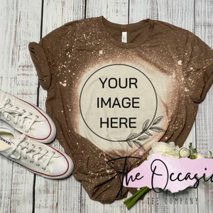 May include: A brown bleached t-shirt with a white circle that says "YOUR IMAGE HERE" and a small branch design. The shirt is on a white wood background with a bouquet of white flowers and two white Converse shoes.