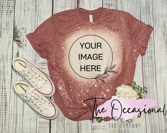 May include: A dusty rose colored t-shirt with a bleached circle in the center. The circle has the text "YOUR IMAGE HERE" inside. The t-shirt is laying on a white wooden surface with a pair of white sneakers and a bouquet of white flowers.