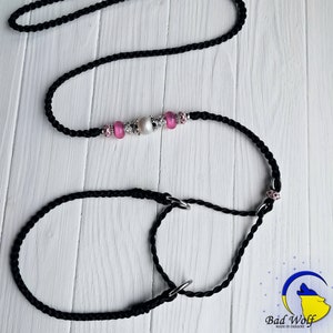 May include: Black braided dog leash with a pink and silver beaded charm. The leash is made of two separate pieces, a longer leash and a shorter loop.