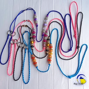 May include: A collection of colorful braided cords with beads and metal rings. The cords are in various colors, including pink, blue, black, and orange. The beads are made of glass and are in various colors, including purple, pink, and black. The metal rings are silver and are used to connect the cords.