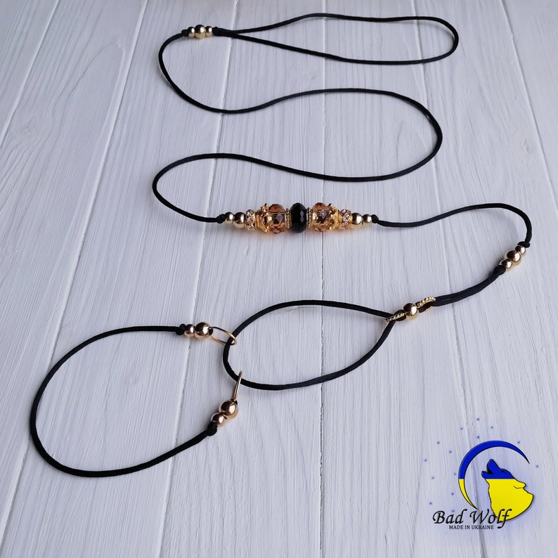 May include: Black and gold dog leash with a beaded accent. The leash is made of two separate pieces, a shorter loop and a longer strap. The beaded accent features gold beads and a black gemstone.