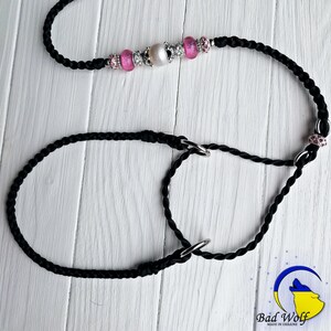 May include: Black braided dog leash with a silver clasp and pink and silver beads. The leash has a loop on one end and a ring on the other end.