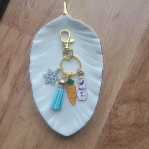 May include: A gold keychain with a blue tassel, a carrot charm, a snowflake charm, and a snowman charm.