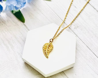 Könnte beinhalten: Eine zarte goldene Blattkette mit einem goldenen Anhänger. Der Anhänger ist eine detaillierte Ausschneidung eines Blattes mit einem filigranen Design.