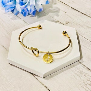 Könnte beinhalten: Goldenes Knoten-Armband mit einem kleinen Anhänger mit dem Buchstaben J.