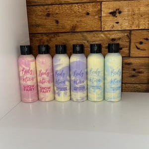May include: Six small bottles of body lotion with different scents. The bottles are clear and have black lids. The labels are white with purple and pink text. The scents are Snow Fairy, Jamaican Me Crazy, and Pink Island Waters.
