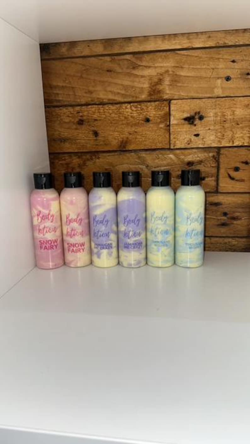 May include: Six small bottles of body lotion with different scents. The bottles are clear and have black lids. The labels are white with purple and pink text. The scents are Snow Fairy, Jamaican Me Crazy, and Pink Island Waters.