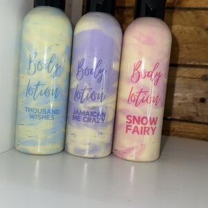 May include: Three bottles of body lotion with different scents. The bottles are white with swirls of blue, purple, and pink. The labels are pink and say "Body Lotion" with the scent name below. The scents are "Thousand Wishes", "Jamaican Me Crazy", and "Snow Fairy".