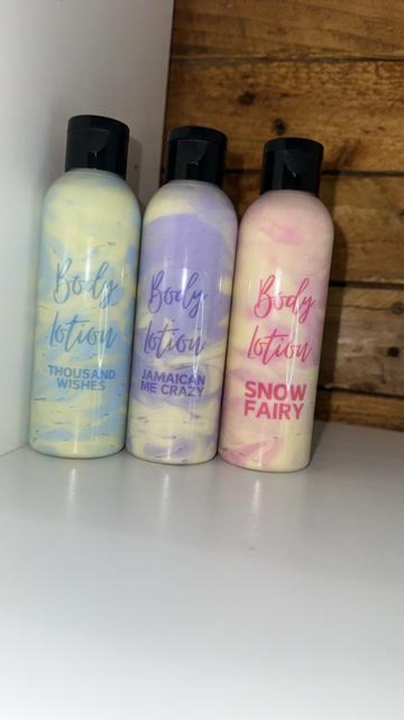 May include: Three bottles of body lotion with different scents. The bottles are white with swirls of blue, purple, and pink. The labels are pink and say "Body Lotion" with the scent name below. The scents are "Thousand Wishes", "Jamaican Me Crazy", and "Snow Fairy".