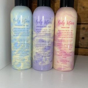May include: Three bottles of body lotion with different scents: Thousand Wishes, Jamaican Me Crazy, and Snow Fair. The bottles are clear with a swirl of color inside. The labels are white with black text.